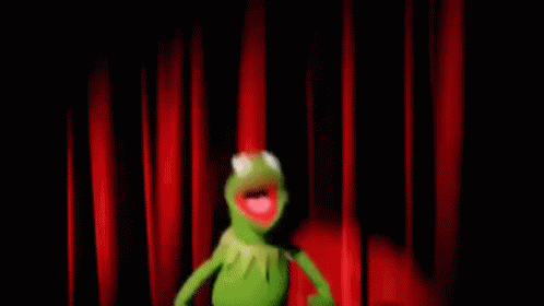 Kermit the frog waving arms frantically in front of a red theatre curtain and running off stage