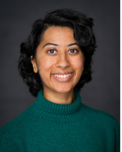 Mythri is an Indian American woman with short, wavy, black hair, wearing a sea green turtleneck, smiling to the camera.