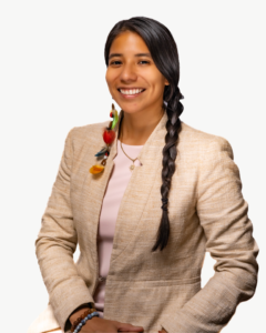 Yura is an Indigenous Kichwa Ecuadorian and Colombian woman with long braid, wearing a beige jacket; she's smiling to the camera.